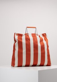 Borsa tote grande con strisce verticali arancioni e crema. Realizzata in tessuto resistente, presenta una maniglia metallica e una chiusura con bottone a scatto.