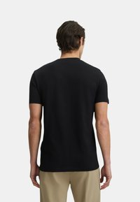 T-shirt nera a maniche corte in cotone, con colletto rotondo semplice, vestibilità ampia e superficie liscia. Nessun motivo o grafica visibile.