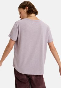 Licht lavendelkleurig t-shirt met korte mouwen, een ontspannen pasvorm, ronde halslijn en opgerolde mouwen. Zachte textuur en gladde afwerking.
