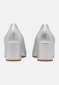 Chaussures à talons hauts argentées avec une finition texturée et un talon carré. Les chaussures présentent un design à bout pointu et une silhouette lisse.