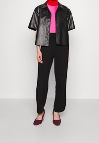 Zwart imitatieleren shirt met korte mouwen, felroze geribbelde trui, zwarte broek met zijdetails en bordeauxrode geweven hoge hakken.