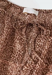 Tissu imprimé léopard marron et beige avec un cordon noué en nœud et une taille élastique avec une étiquette visible.