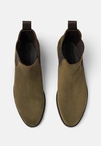 Botines de ante verde oliva con una textura suave, paneles laterales elásticos y lengüetas para facilitar su colocación. Suelas de goma planas.