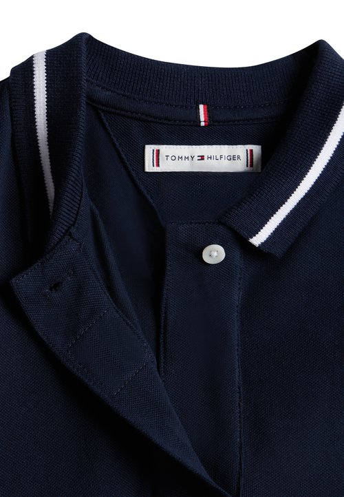 Polo bleu marine en tissu texturé, avec un col et une patte de boutonnage, rehaussé de rayures blanches sur le col. Étiquette Tommy Hilfiger visible.