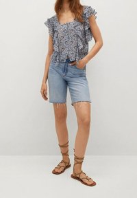 Modrá blůza s květinovým vzorem a volánkovými rukávy, doplněná světle modrými roztrhanými džínovými šortkami. Celý outfit dokončují hnědé sandály na řemínky.