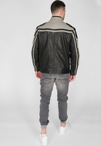 Svart och grå läderjacka med en slät yta, med två horisontella ränder längs axlarna och vaddering vid armbågarna.