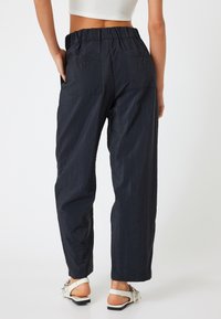 Zwarte, lichte, gestructureerde broek met een elastische tailleband en twee achterzakken. Gecombineerd met witte sandalen met een decoratief accent.