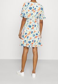 Blommig klänning i ljusblått med flerfärgad mönster. Korta ärmar, figursydd midja, utsvängd kjol och volangkanter på ärmarna. Bärs med vita sneakers.