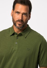Grøn polo t-shirt lavet af tekstureret stof, med krave, en to-knap lukning og et diskret logo på brystet.