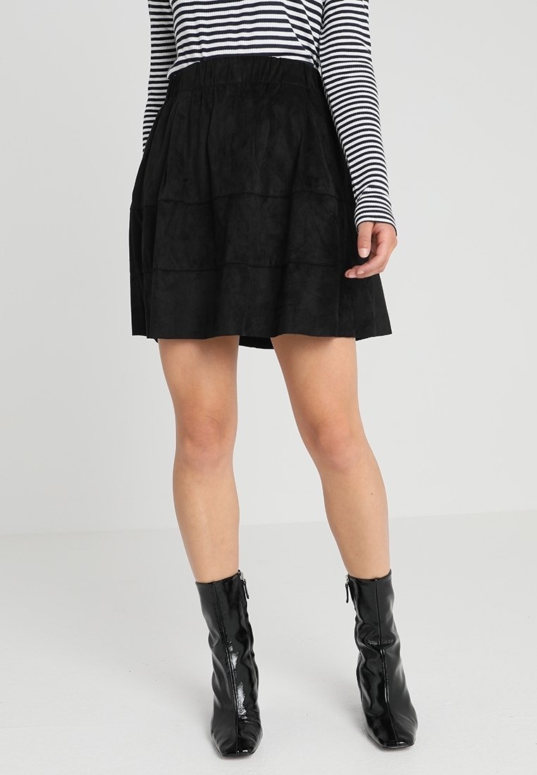 Zwarte suède rok met gelaagd ontwerp, voorzien van een elastische tailleband. Gecombineerd met glanzende zwarte enkellaarzen voor een elegante uitstraling.