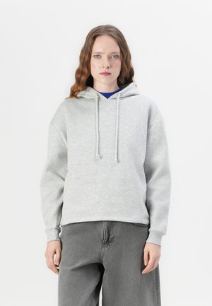 Sudadera con capucha gris de corte holgado, con cordones y puños acanalados, acompañada de jeans grises casuales. Textura suave, diseño sencillo.