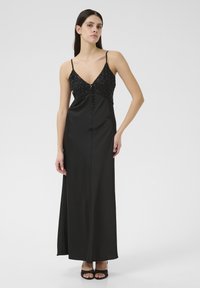 Robe maxi en satin noir avec un corsage perlé, décolleté en V et fines bretelles. Texture lisse avec des boutons décoratifs sur le devant.