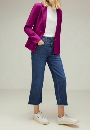 Blazer magenta, top blanc, jean cropped bleu avec ourlets effilochés, et baskets blanches avec semelles beiges. Tenue décontractée sur un fond uni.