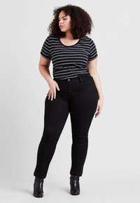 Stripet svart og hvit t-skjorte med U-hals, kombinert med svarte skinny jeans og svarte ankelboots. Jevn stofftekstur.