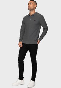 Grauer Strick-Polo mit langen Ärmeln und Kragen, mit einem kleinen gestickten Logo. Kombiniert mit schwarzen Slim-Fit-Hosen und weißen Sneakers.