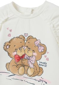 Witte katoen shirt met een graphic van twee bruine teddyberen met strikken. Vergezeld van roze decoratieve harten en de tekst "Lieve beren!"