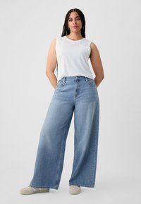Lichtblauwe wijde jeans met een mid-rise pasvorm, gecombineerd met een wit mouwloos topje. Zachte denimtextuur, minimale zichtbare stikdetails.