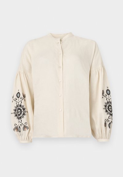 Κρεμ μπλούζα από λινό με μανδυρίνο λαιμό, μπροστινά κουμπιά και φουσκωτά μανίκια με μαύρη και πολύχρωμη λουλουδάτη κεντητική.