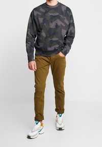 Szary bluza w kamuflażu z okrągłym dekoltem, zestawiona z khaki spodniami i białymi trampkami z akcentami w kolorze turkusowym i żółtym.