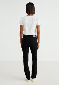 Jeans negros ajustados con una cintura de tiro medio, tela de mezclilla elástica y una etiqueta de marca azul en la cinturilla trasera. Combinados con una camiseta blanca.