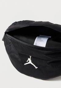 Musta nylonista valmistettu vetoketjullinen laukku. Ominaisuuksina valkoisella kirjailtu Jumpman-logo. Sisäpuoli näkyvissä, jossa hoito-ohjetarra. Pehmeä tekstuuri.