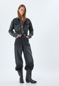 Svart denimskjorta med två bröstfickor, silverknappar, tillsammans med löst sittande svarta jeans och svarta cowboyboots med dekorativ sömnad.