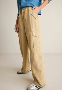Beige cargo bukser med elastisk talje, sidelommer og en løs pasform. Materialet virker let og har en subtil tekstur.