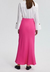 Fuchsiafarbener langer Maxi-Rock mit strukturierter Oberfläche, kombiniert mit einem weißen Hemd mit durchgehender Knopfleiste, breiten Manschetten und goldenen Knöpfen. Schwarze Schuhe.