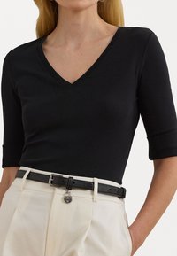Zwarte v-hals top met driekwart mouwen. Gladde stof met een aansluitend ontwerp, gecombineerd met hoge crèmekleurige broeken en een zwarte riem.