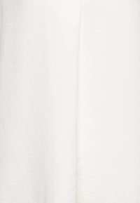 Bílá tkanina, mírně strukturovaná s lehkým a vzdušným charakterem. Hladký povrch s přirozenými nepravidelnostmi, bez viditelných vzorů nebo hardwaru.