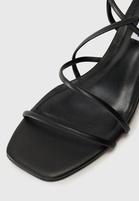 Sorte lær sandaler med tynne buede stropper, firkantet tådesign og en glatt teksturert såle. Minimalsitisk stil, passende for forskjellige anledninger.