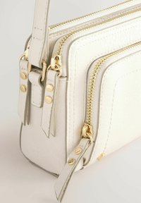 Bolso cruzado blanco hecho de material sintético texturizado. Cuenta con cremalleras doradas, detalles en metal y múltiples compartimentos con cremallera.