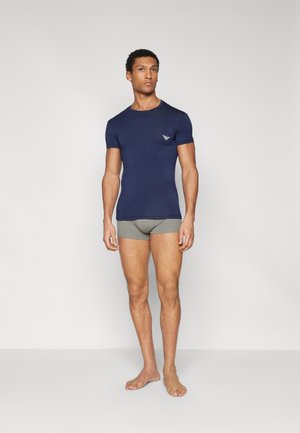 T-shirt corto blu navy realizzato in materiale morbido con un design aderente e un piccolo logo sul petto, abbinato a slip grigi chiari.