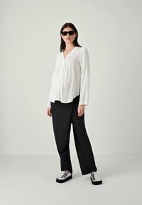 Blusa bianca con pieghe verticali, abbinata a pantaloni neri larghi e scarpe platform argento. Gli occhiali completano l'outfit.
