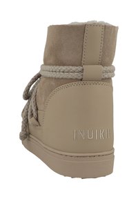 Beige mockaskhäl med en mjuk foder, flätade snören och stygn detaljer; har en logotyp bak och en platt sula.