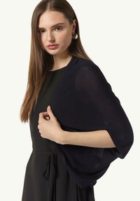 Marineblaues leichtes Tuch, das über einem schwarzen Kleid drapiert ist. Der Stoff ist durchsichtig mit einer weichen Textur, hat weite Ärmel und eine lockere Passform.