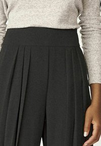 Černé plisované kalhoty s vysokým pasem, vyrobené z měkké tkaniny, s ostrými záhyby pro strukturu a hladkou texturou.