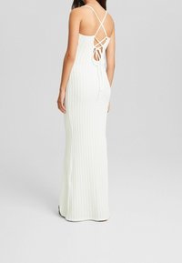 Robe maxi blanche côtelée avec une coupe ajustée, dos ouvert avec des bretelles croisées et un détail noué à la taille.