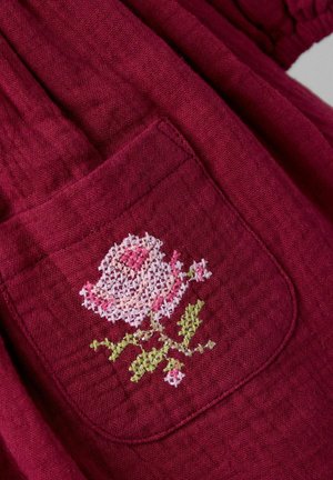 Burgunderfarbene Stoff hat eine Tasche mit einer gestickten rosa Rose und grünen Stielen, die eine strukturierte Oberfläche und detaillierte Nähte zeigt.