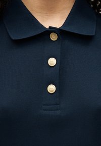 Polo bleu marine avec une texture côtelée, présentant un col à revers et trois boutons dorés sur la patte de boutonnage.