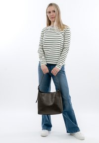 Czarna skórzana torebka w zakrzywionym kształcie z górnym uchwytem, wzbogacona o gładką fakturę. Model w paskowanej bluzce z długim rękawem i dżinsach.