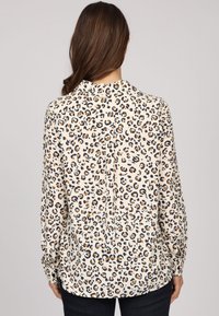 Chemise à manches longues de couleur crème avec un imprimé léopard noir et marron, à coupe décontractée et avec un discret plissage au dos.