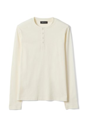 Maglietta Henley a maniche lunghe color crema con quattro bottoni e scollo rotondo, posata distesa su uno sfondo bianco.