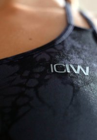 Μαύρο αθλητικό μπλουζάκι με υφή, με κοντινή άποψη που εμφανίζει το λογότυπο ICIW σε ανοιχτό γκρι πάνω στο ύφασμα.