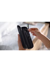 Custodia da viaggio nera con uno spazzolino elettrico nero e uno spazzolino con setole blu-verdi, tenuti da una mano. La custodia ha un design elegante.