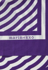 Lilla og hvit mønstret stoff har dristige bølgede striper, med merkevarenavnet "marimekko" trykt nær bunnen. Glatt tekstur.