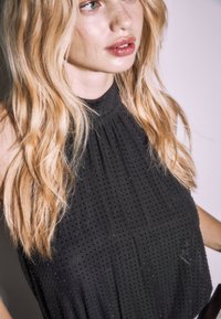 Zwarte mouwloze top met een hoge hals, voorzien van subtiele textuurdetails en een geplooid ontwerp, nauwsluitend rond het lichaam.