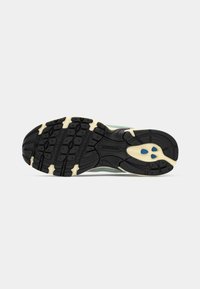 Semelle en caoutchouc noire et crème de chaussure de course avec des accents bleus et un motif texturé pour l'adhérence, vue par le dessous sur fond clair.