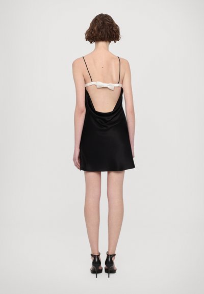 Abito in satin nero con drappeggio morbido, schiena scoperta e spalline sottili. Decorato con un accento in fiocco bianco sul retro.
