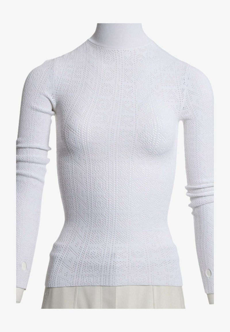 Pull col roulé blanc à manches longues avec motifs géométriques perforés, porté sur un mannequin avec un pantalon clair.